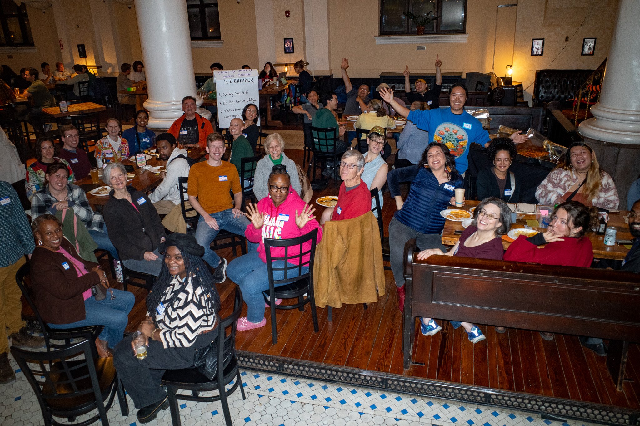 A large group of community builders gathered around dinner tables, cheering